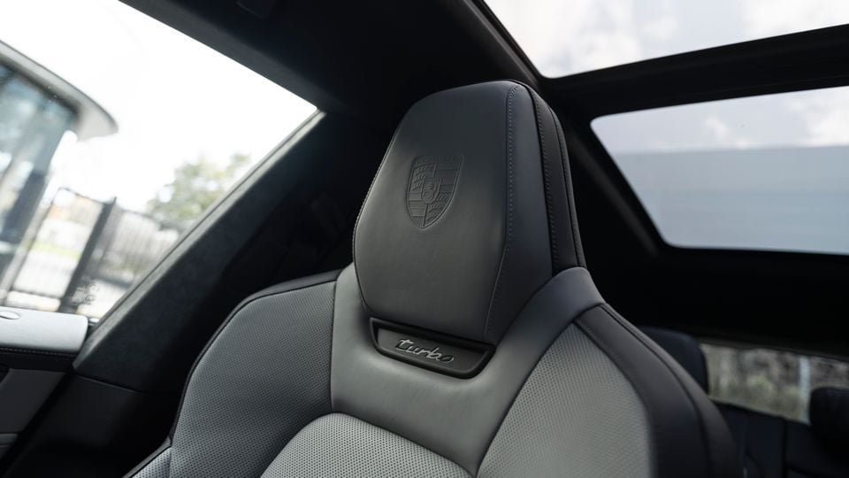 Porsche Cayenne Turbo leather front seat headrest with embossed Porsche crest and 'turbo' badge, with panoramic sunroof visible above
