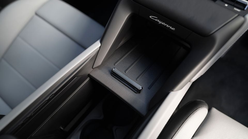Interior view of a Porsche Cayenne centre console storage compartment with a textured carbon-look lid and metal pull handle