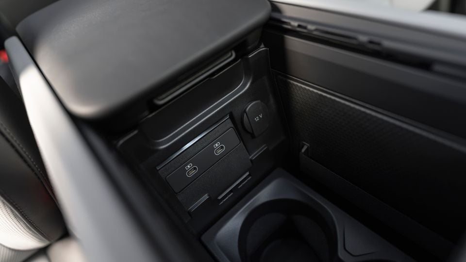 Rear centre console of a Porsche Cayenne Turbo E-Hybrid showing two USB-C charging ports and a 12V power outlet, with a cup holder below