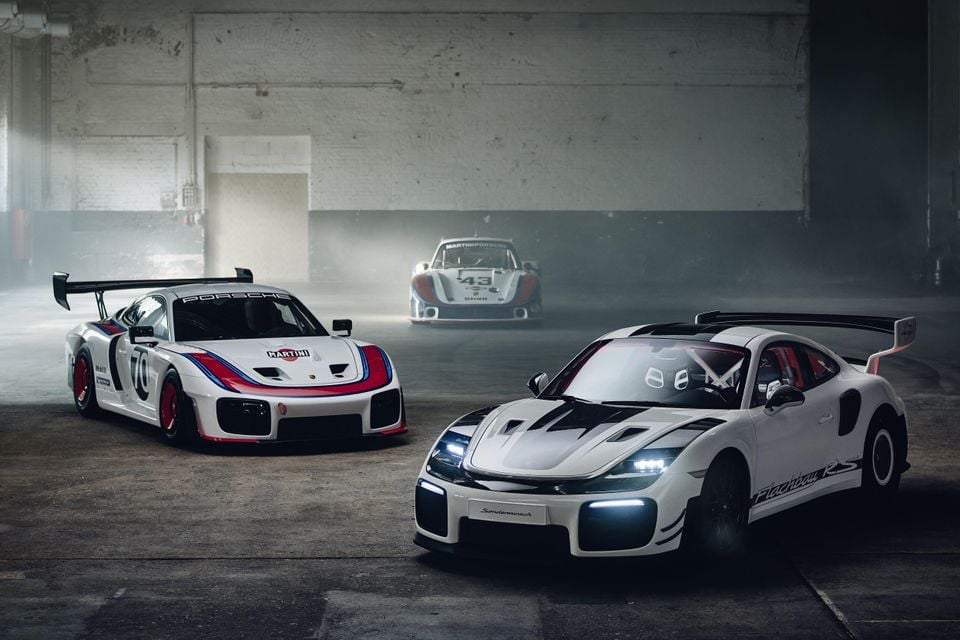 Three Porsche sports cars posed in a misty warehouse, including a Porsche 935 in Martini racing livery, a classic Porsche 935 race car numbered 43 in the background, and a white Porsche 911 GT2 RS Flachbau in the foreground