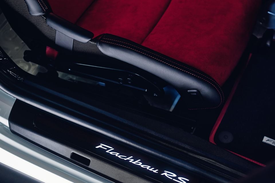 Close-up of the door sill and bucket seat bolster inside a Porsche Flachbau RS, showing red Alcantara upholstery with contrast stitching and a door sill plate inscribed with 'Flachbau RS'
