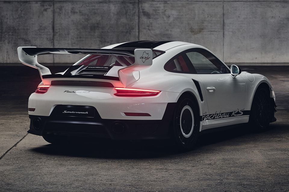 A white Porsche 911 Flachbau RS coupe seen from the rear three-quarter angle, featuring a large rear wing and red interior accents.