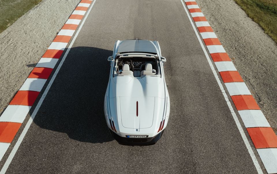 A white Rolls-Royce convertible with its roof down, seen from above parked on a race track marked with red and white kerbing.
