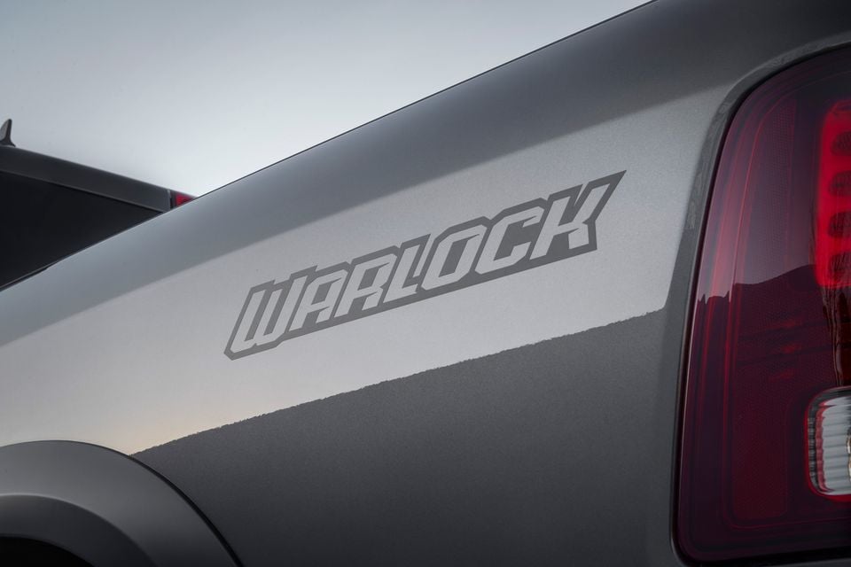 Close-up of the 'Warlock' decal on the tub side of a grey Ram 1500 Warlock ute, with a tail light visible