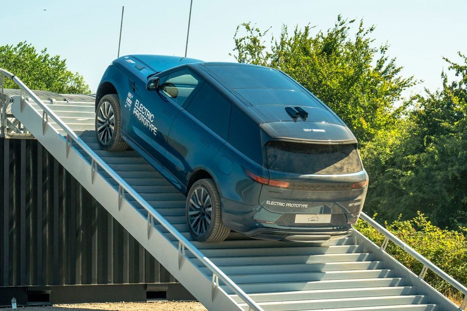 A dark blue Range Rover Sport Electric Prototype SUV climbing a steep ramp during off-road testing, seen from the rear three-quarter angle