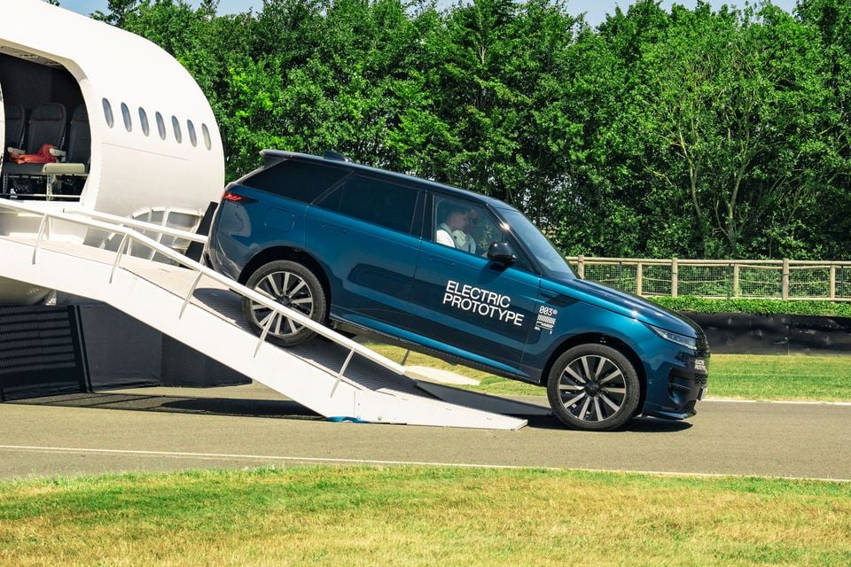 A blue Range Rover Sport Electric Prototype SUV driving down a ramp from a private jet on an airfield