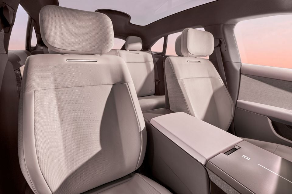 The rear seat interior of a car showing light-coloured upholstered seats with a fold-down centre armrest and panoramic roof