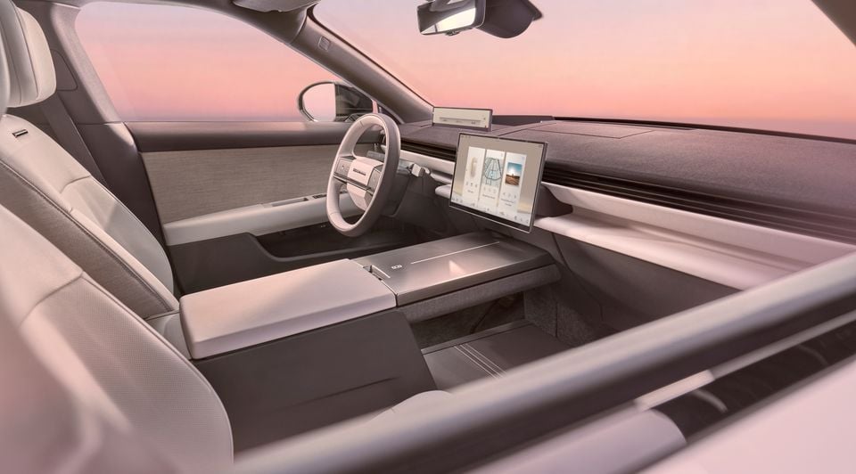 Interior view of a Range Rover GT from the passenger side, showing a minimalist dashboard, large central touchscreen, open centre console, and panoramic windscreen against a sunset sky.