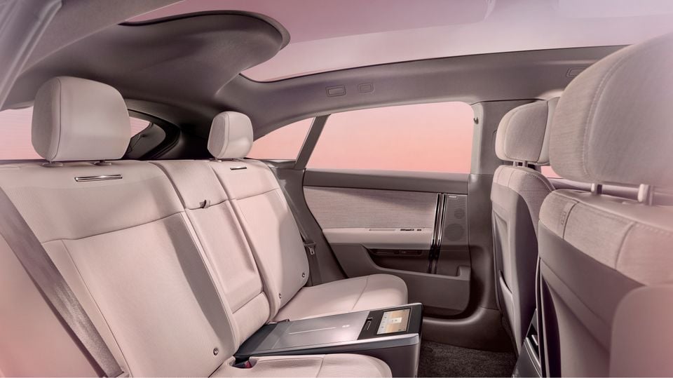 Interior rear seats of the 2027 Range Rover GT showing light-coloured upholstery, a fold-down rear console with a small touchscreen, and a panoramic roofline