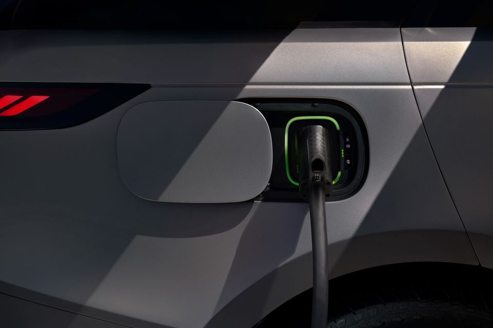 A close-up of a charging cable plugged into the charging port on the side of a silver electric SUV, likely a Range Rover Electric.