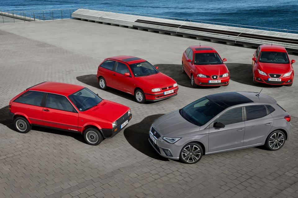 Five generations of the SEAT Ibiza hatchback displayed together on a waterfront plaza, including models from 1984, 1993, 2002, 2008, and a modern grey fifth-generation example in the foreground.