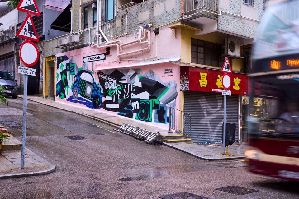 A street mural in Hong Kong featuring a Smart #2 car design with the text 'It's Back' and 'smart', painted on a building wall beside a busy urban street.