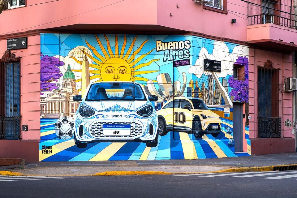 A colourful street mural on a building corner in Buenos Aires depicting two Smart #2 cars with Argentine-themed artwork including a sun, football, and city landmarks, with the text 'Buenos Aires It's Back'