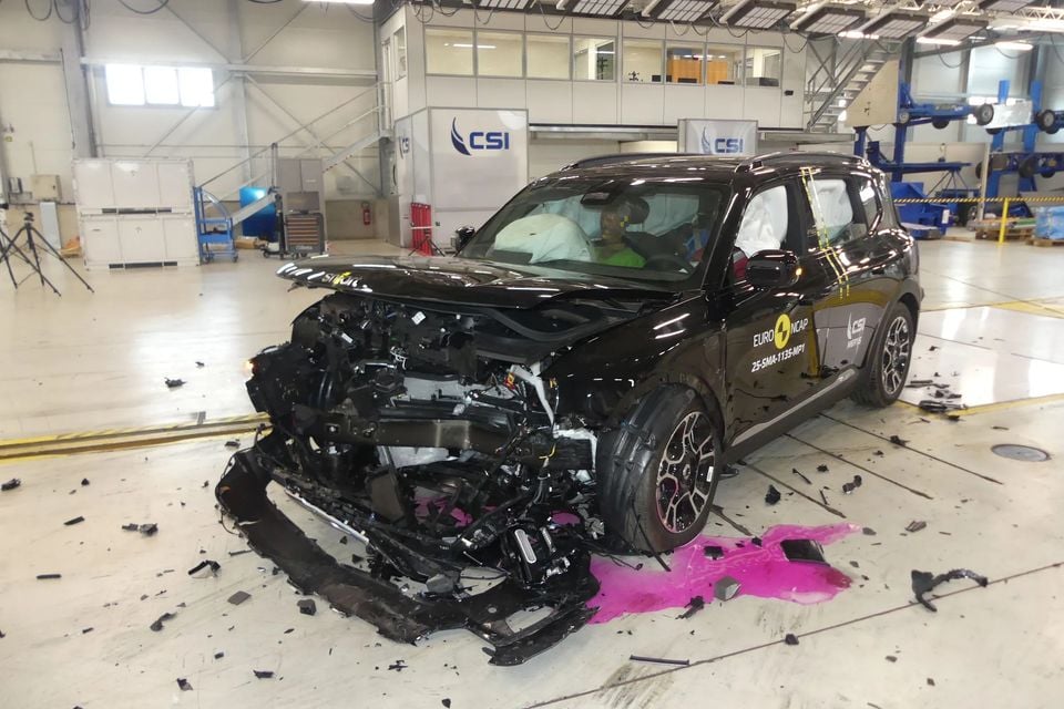 A black Smart #5 SUV after a Euro NCAP frontal crash test, with severe front-end damage and debris scattered on the laboratory floor.