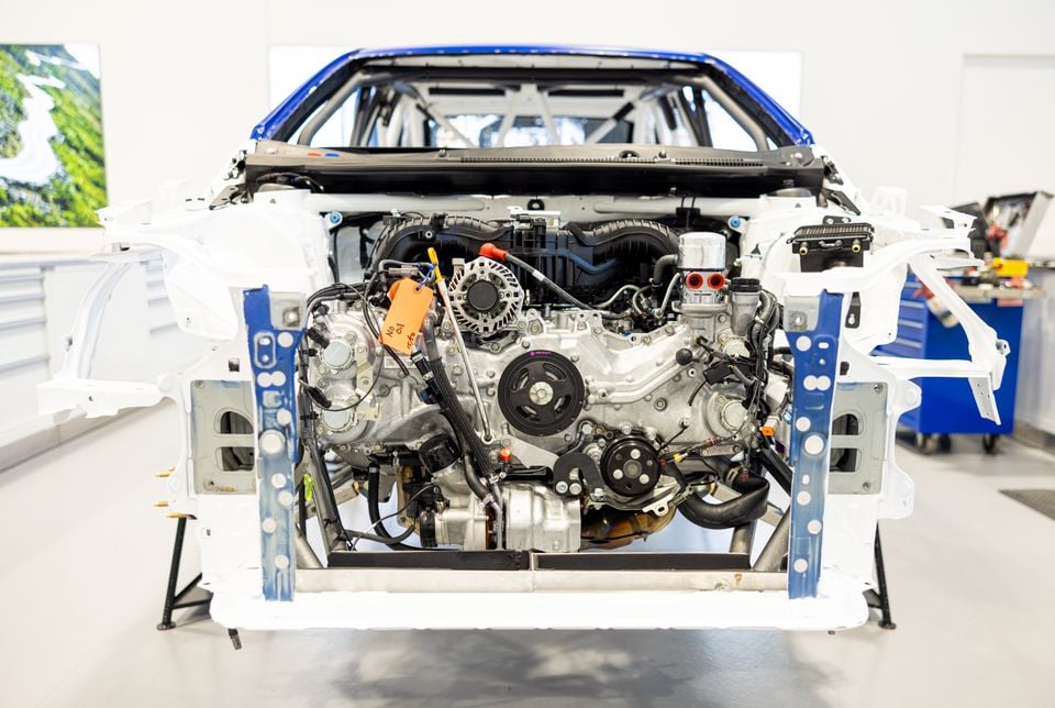 A Subaru FA24 2.4-litre turbocharged boxer engine exposed in a stripped car body shell in a workshop, with a roll cage visible above