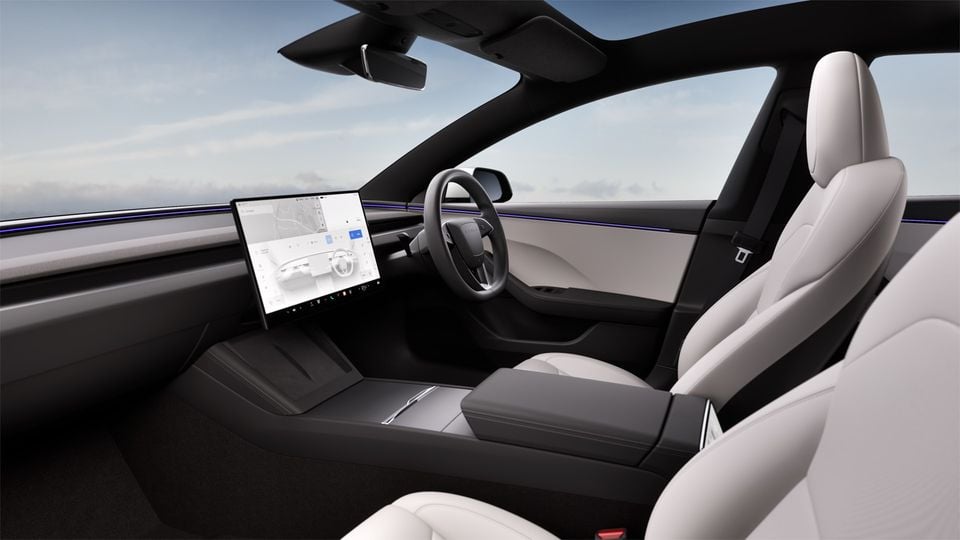 The interior of a Tesla Model 3 showing white leather seats, the steering wheel, and the central touchscreen display.