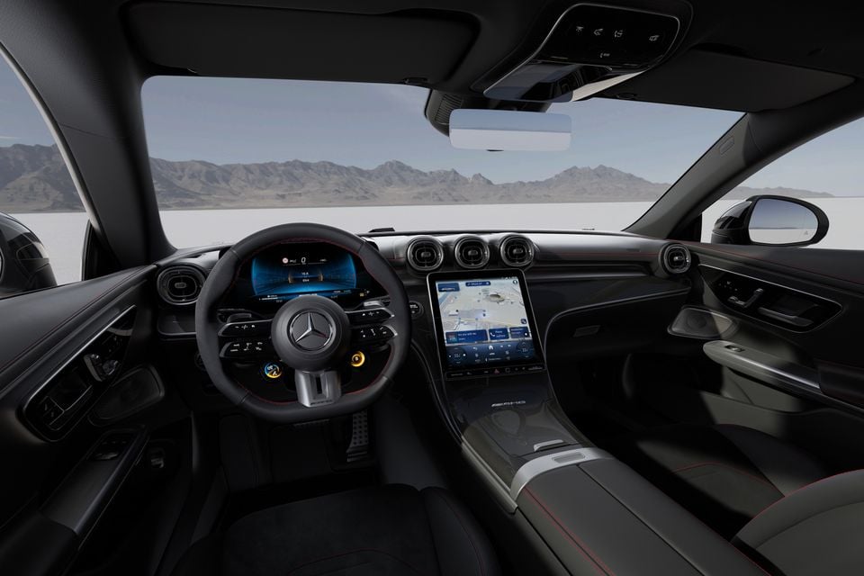 Interior of a Mercedes-AMG CLE 53 showing the AMG flat-bottom steering wheel, digital instrument cluster, large central touchscreen with navigation, and dark cabin trim with red stitching