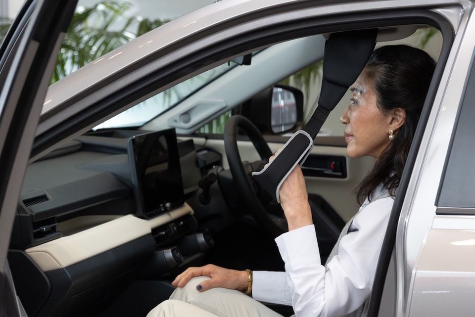 A woman sitting in the driver's seat of a car, holding an assisted entry handle attached to the door frame to help her get in or out
