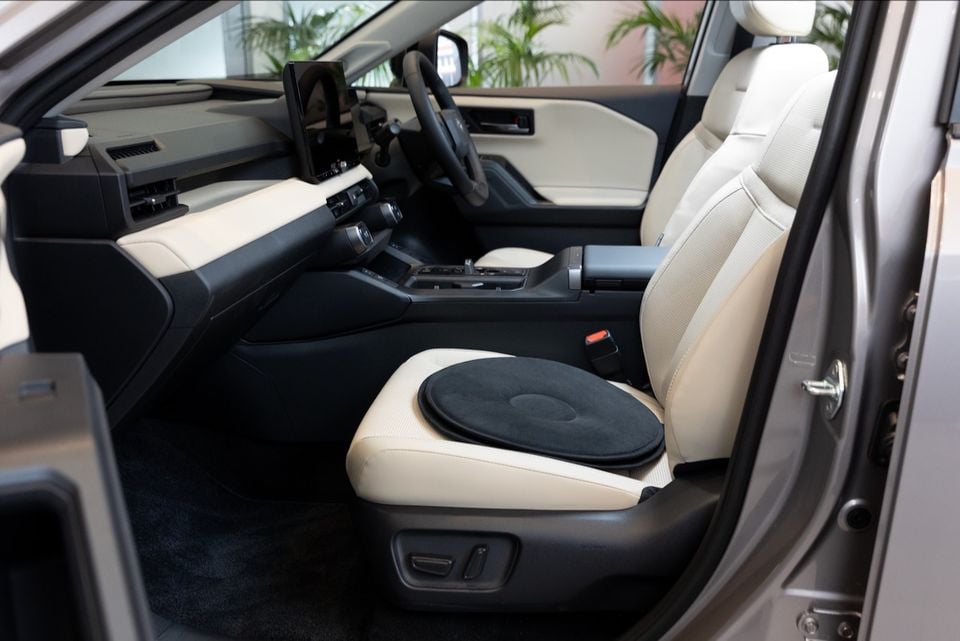 Interior view of a car's front passenger seat with a black swivel cushion placed on it, alongside a two-tone cream and black dashboard and centre console