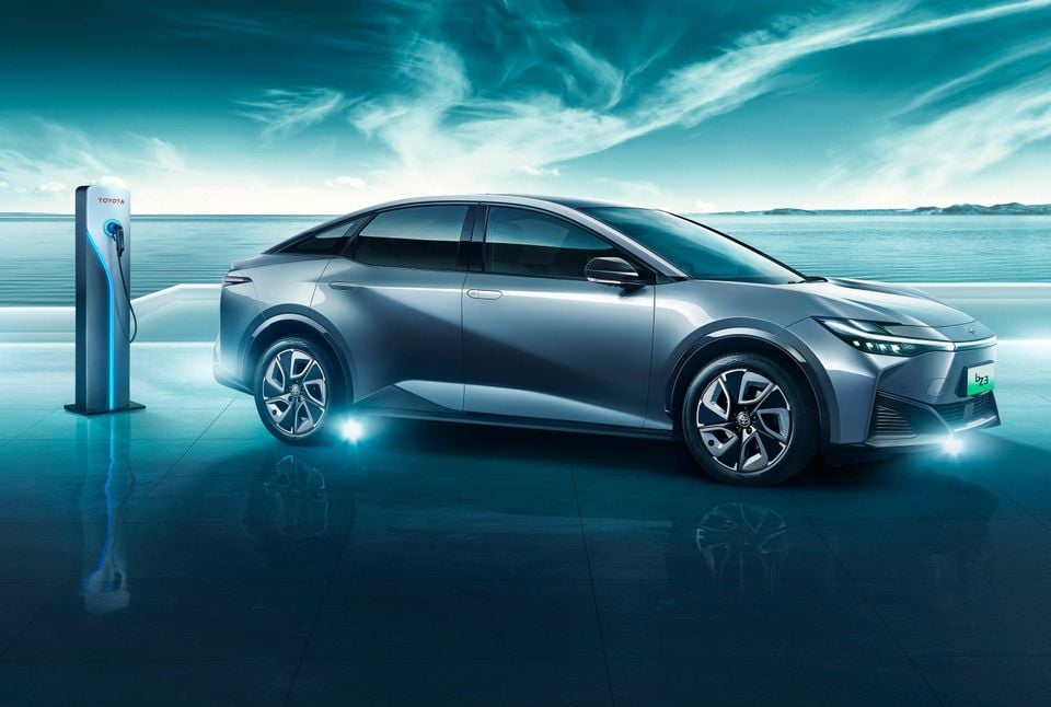 A silver Toyota bZ3 electric sedan parked beside a charging station near the water, viewed from the front side.