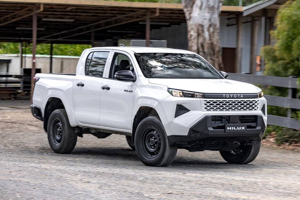 A white 2024 Toyota HiLux Workmate dual-cab ute photographed from the front quarter view parked on a gravel driveway.