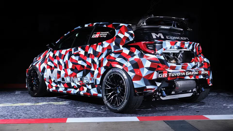 Toyota GR Yaris M Concept em camuflagem geométrica vermelha, branca e preta com pintura Toyota Gazoo Racing, visto do ângulo traseiro de três quartos