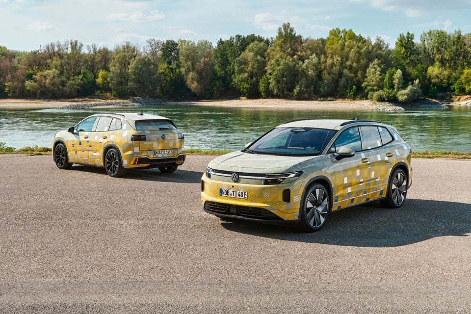 Two camouflage-wrapped Volkswagen ID. Tiguan prototype SUVs parked beside a river, one shown from the front and one from the rear.