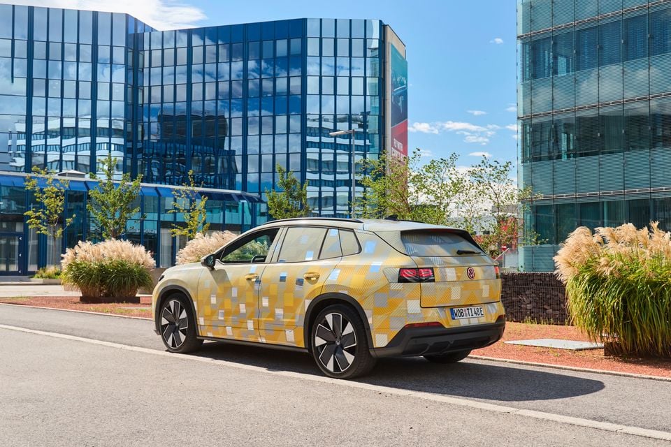 A camouflage-wrapped Volkswagen ID. Tiguan prototype SUV parked on a street in front of glass office buildings, viewed from the rear quarter.