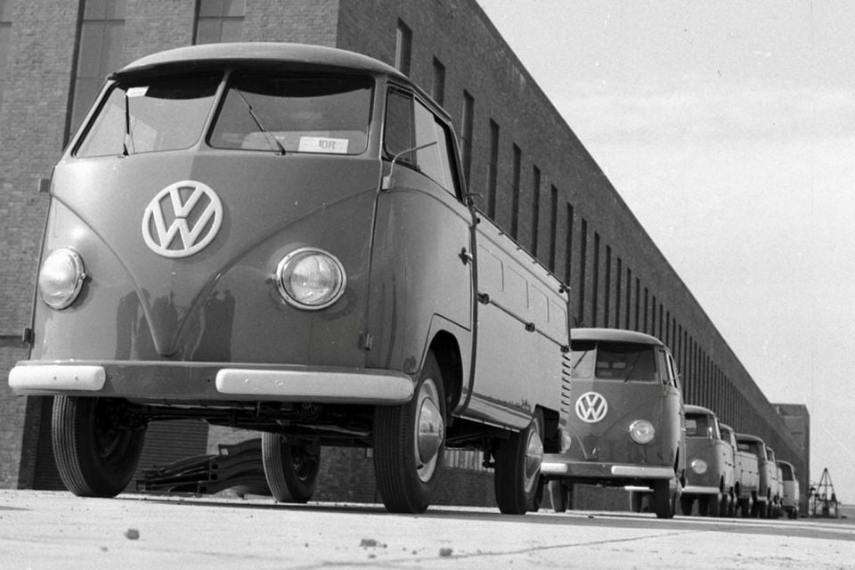 A row of Volkswagen Type 2 (T1) single-cab pickup trucks parked outside a factory building, seen from the front in a vintage black-and-white photograph.