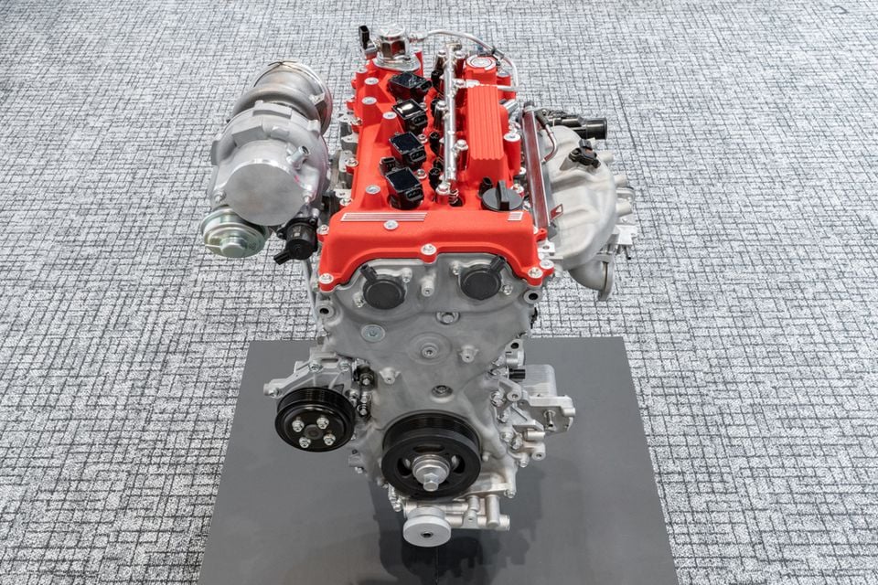 Um motor em linha turboalimentado com uma tampa de came vermelha exibida em um suporte, mostrado de cima