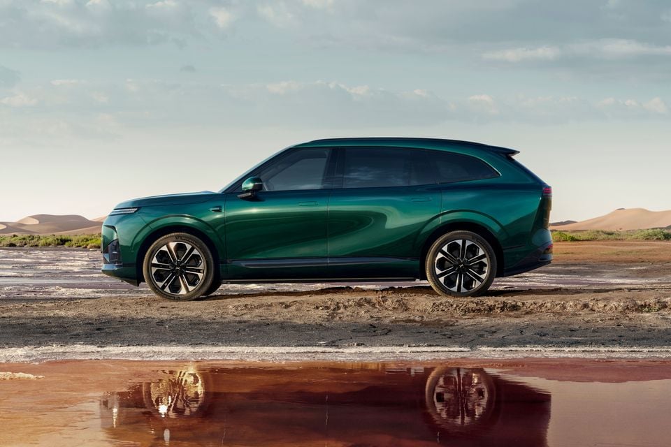 A green XPeng G9L SUV shown side-on, parked on a salt flat beside a reflective pool with desert sand dunes behind