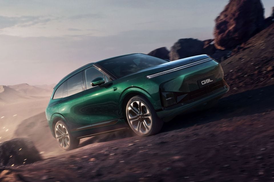 A green XPeng G9L large SUV driving up a dusty, rocky desert slope at dusk, seen from the front three-quarter angle