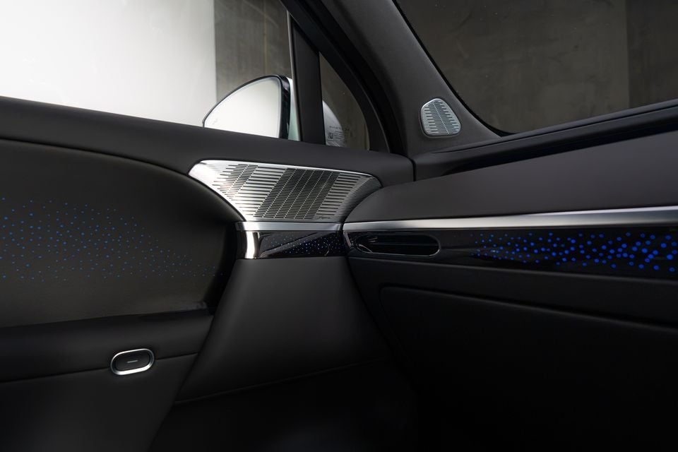 Front door trim of the Xpeng G9 with metal speaker grilles and blue dotted ambient lighting across the door and dashboard