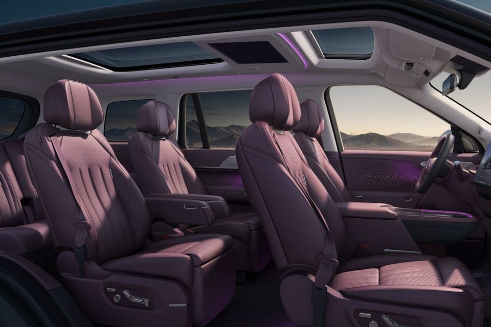 Interior side view of the XPeng G6 SUV showing three rows of purple-toned fabric seats with ambient lighting and a panoramic sunroof