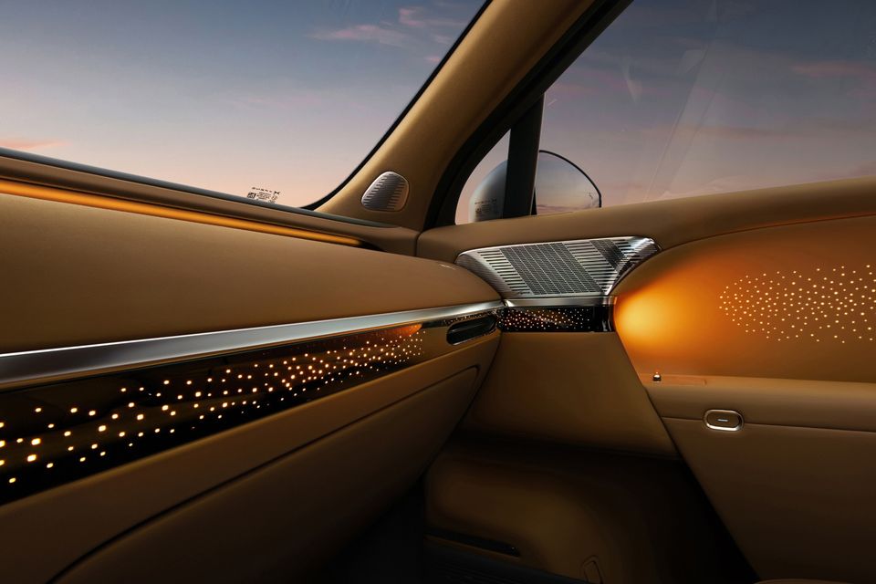 Interior door panel of the Xpeng G6 featuring ambient star-pattern lighting, tan leather trim, and a chrome speaker grille at dusk