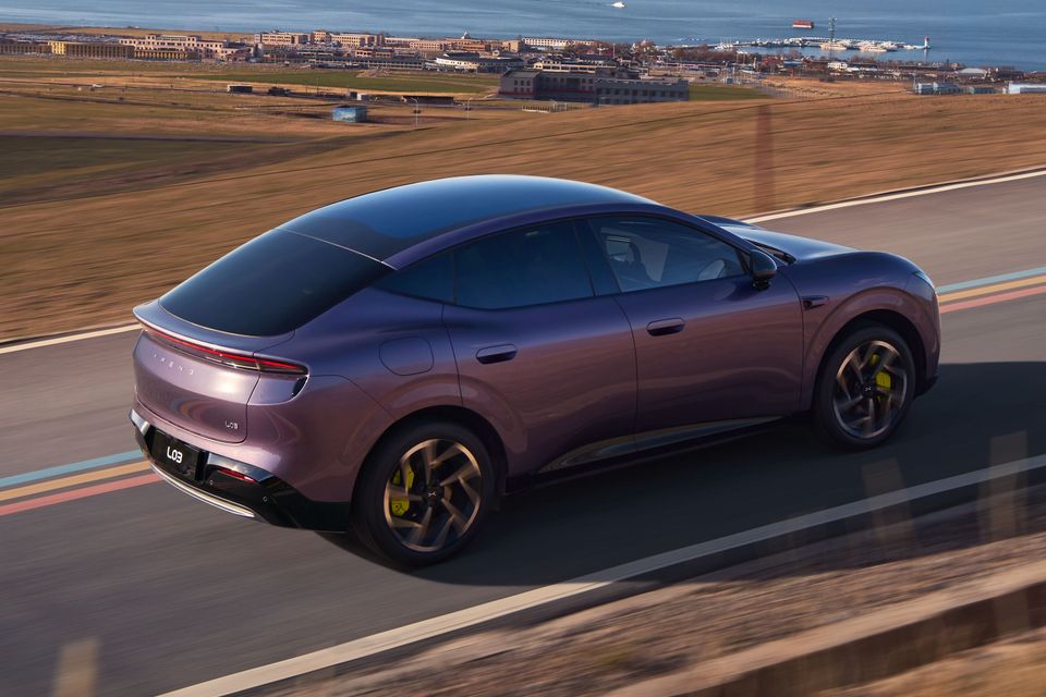 A purple Xpeng L03 sedan driving on a coastal highway, seen from an elevated rear angle