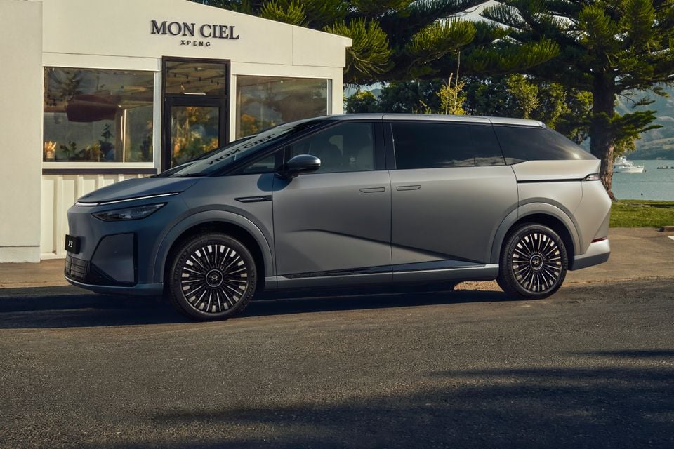 An Xpeng X9 electric people mover in grey, seen from the side, parked outside a Mon Ciel Xpeng showroom near the waterfront.