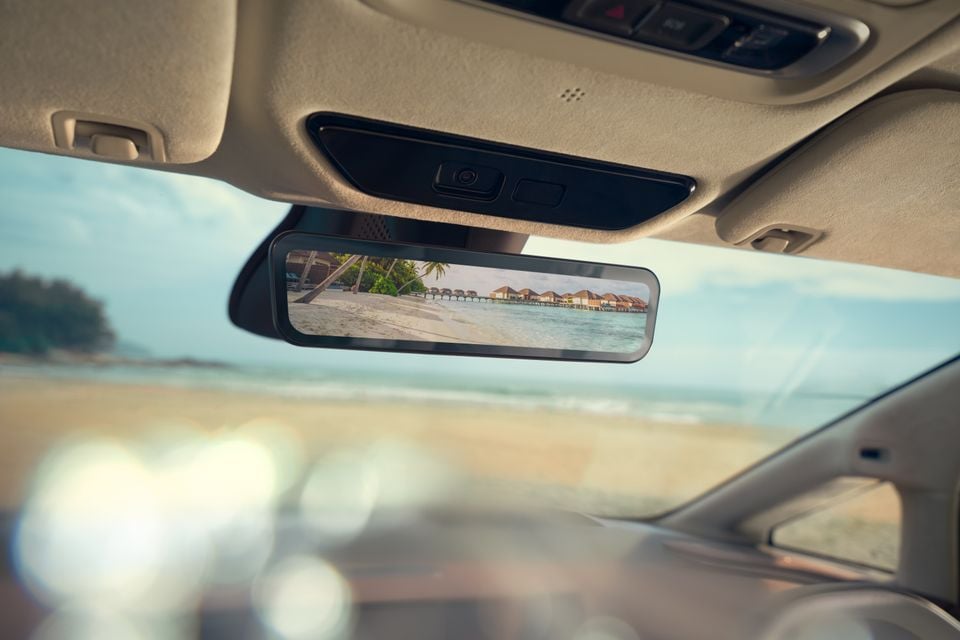 A digital rear-view mirror inside a car displaying a tropical beach scene with overwater bungalows and palm trees