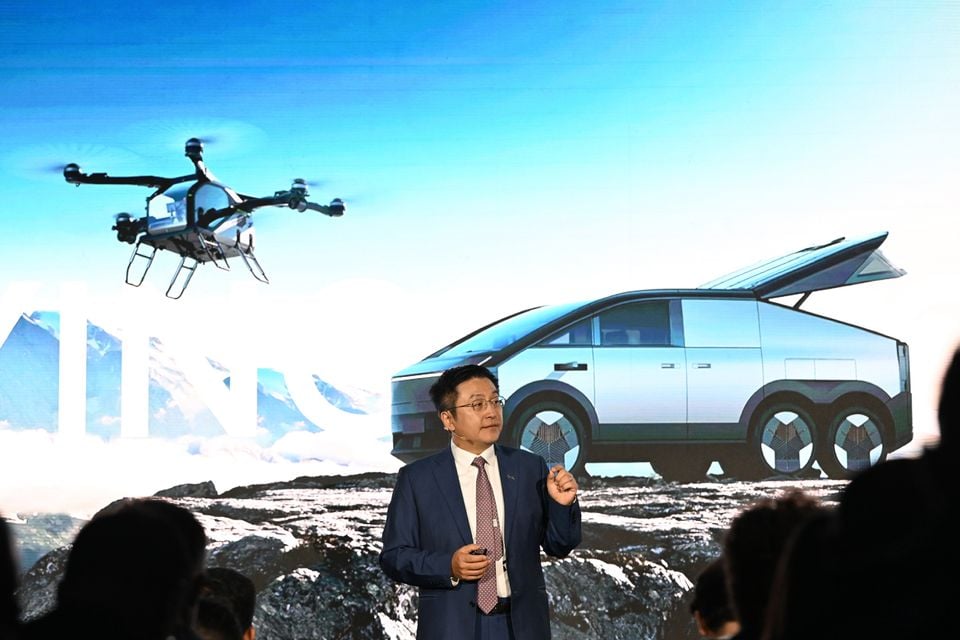 A presenter speaks on stage in front of a large display showing a futuristic electric ute concept and a drone at what appears to be an Xpeng product event.