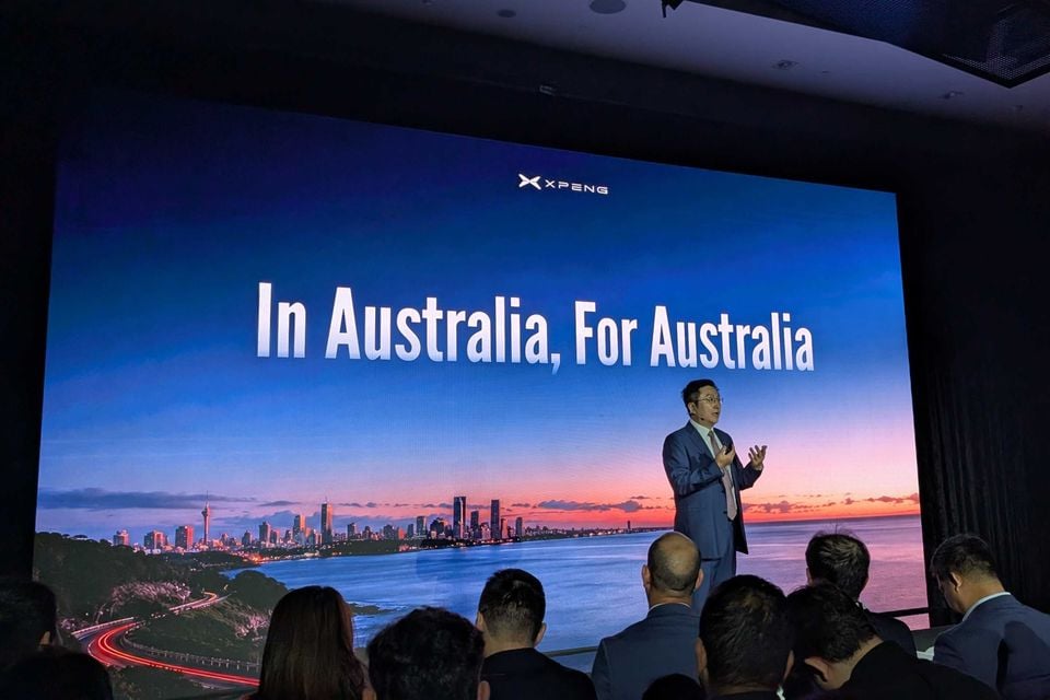 A presenter speaks on stage at an Xpeng Australia launch event, with a large screen behind him displaying the text 'In Australia, For Australia' and the Xpeng logo, in front of an audience.