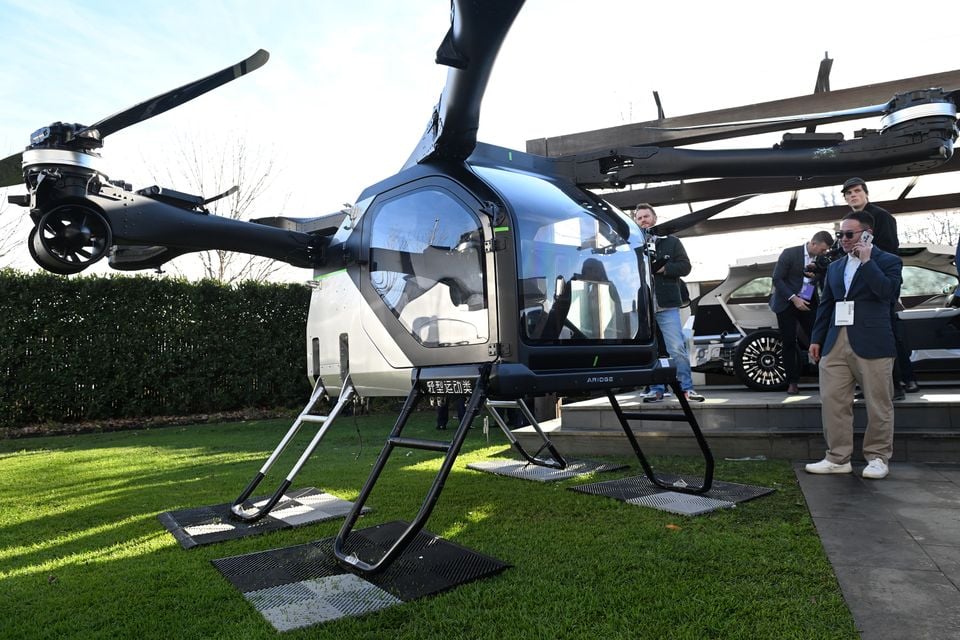 An Xpeng eVTOL flying vehicle on display on a grass lawn at an outdoor event, with onlookers standing nearby