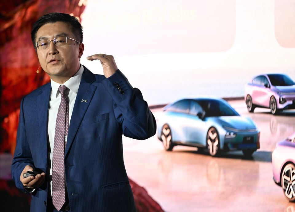 An XPeng executive presenting on stage, gesturing in front of a screen displaying XPeng electric concept vehicles.