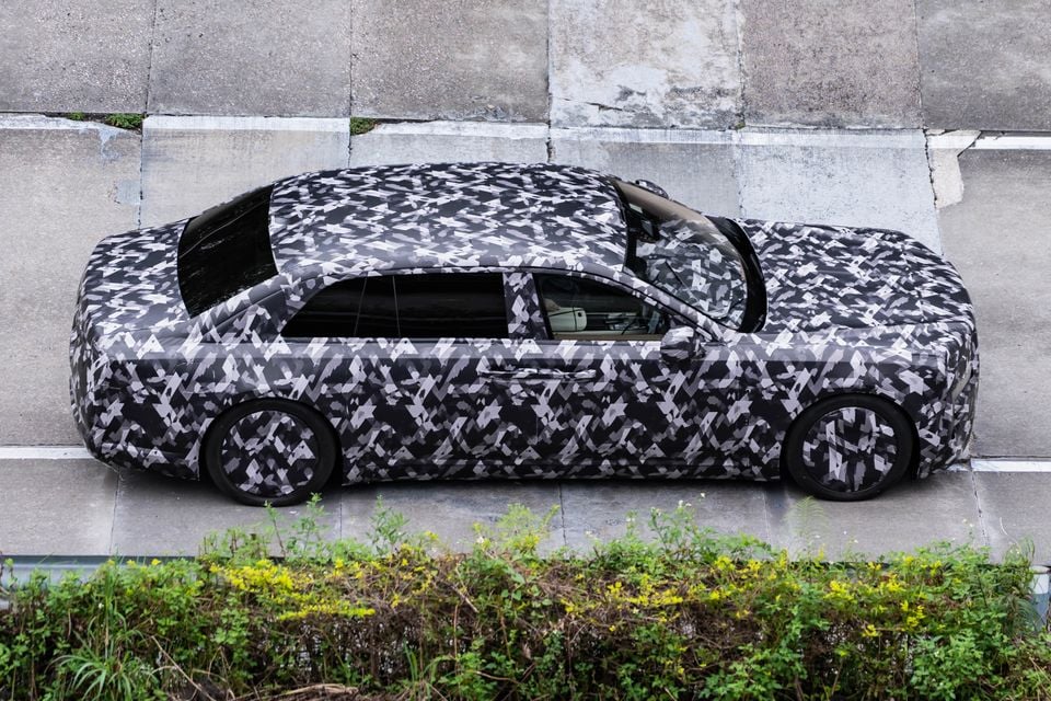 A camouflage-wrapped prototype sedan, possibly a Yangwang, parked on a street, seen from above in profile