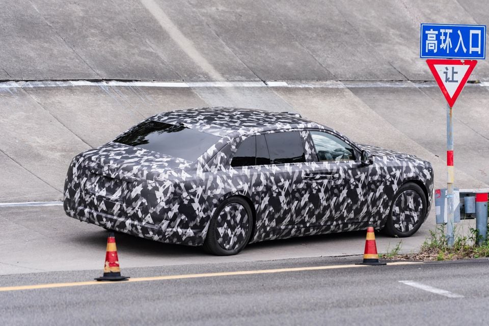 A camouflage-wrapped prototype sedan, believed to be a Yangwang model, seen from the rear quarter on a test track in China.