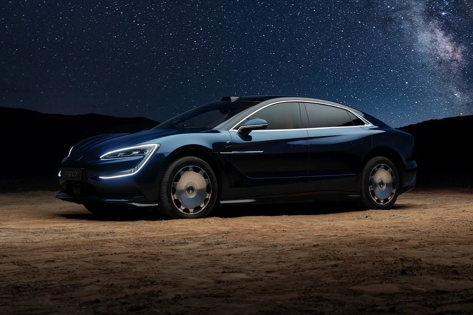 A dark blue Yangwang U7 sedan parked on desert sand at night under a starry sky, seen from the front side angle.