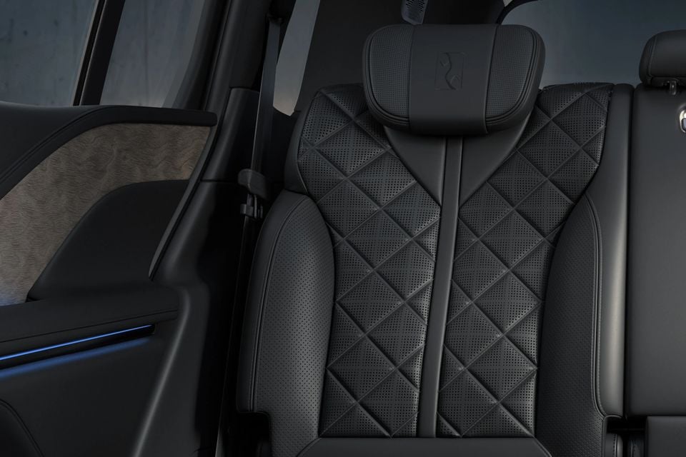Black quilted, perforated leather rear seat with an embossed headrest logo inside the Yangwang U8, beside a door with blue ambient lighting