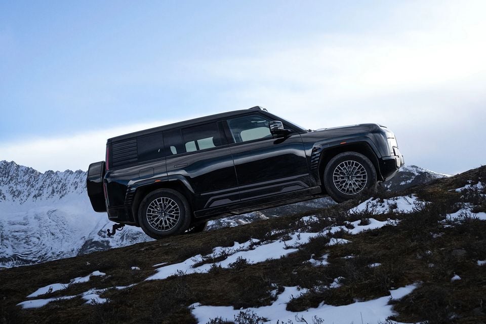 A black Yangwang U8 SUV seen side-on, climbing a steep snowy hillside with snow-capped mountains behind