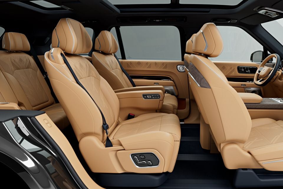 Tan leather interior of a Zeekr 9X SUV showing three rows of seats with quilted detailing, seat controls, and a panoramic sunroof overhead