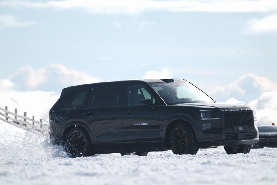 A black Zeekr SUV driving through snow, seen from the front-side