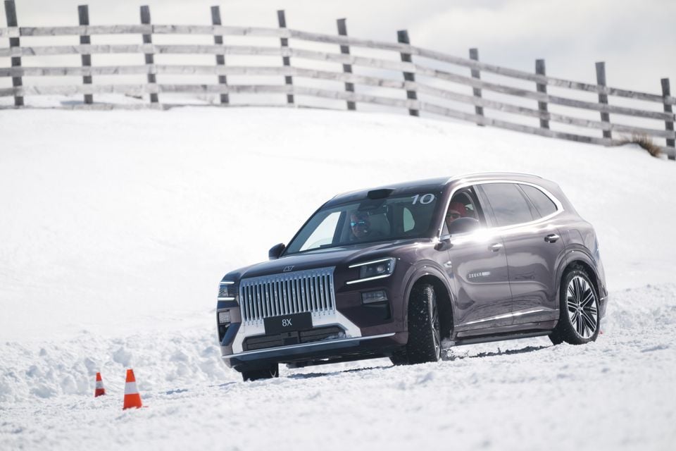 A Zeekr 8X SUV being driven on a snow-covered track with traffic cones, seen from the front side